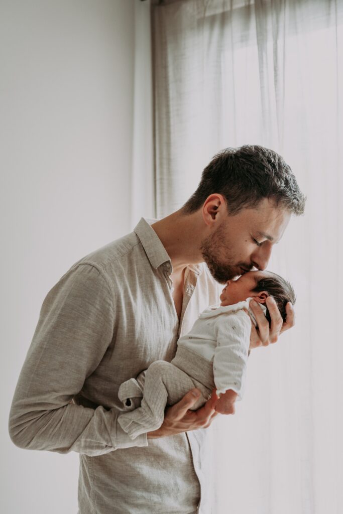 Vader houdt baby vast en kust newborn baby op voorhoofd