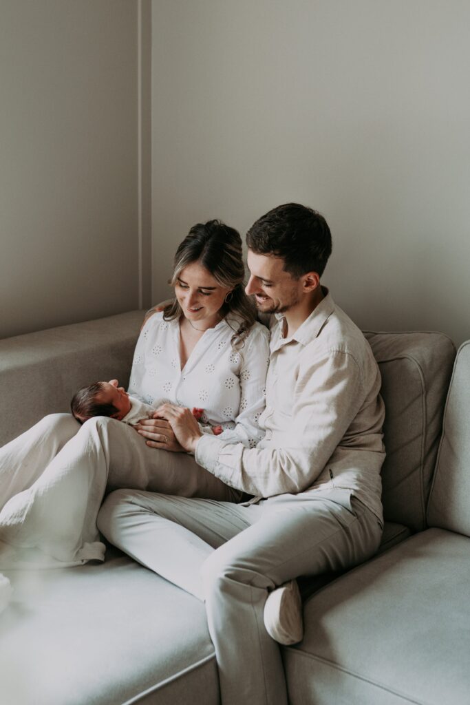 Vader en moeder zitten op bank en kijken naar newborn baby