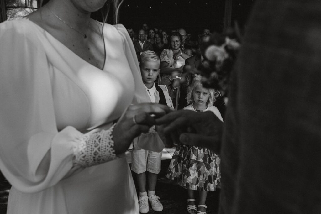 Bruidspaar schuift ringen om elkaars handen en de ringendragers kijken hiernaar