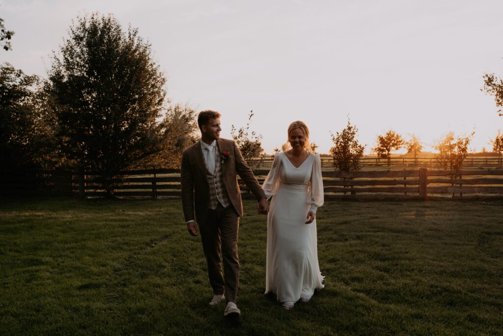 Bruidspaar loopt hand in hand in weiland tijdens golden hour