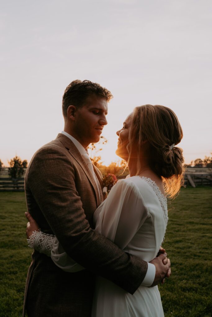 bruidspaar houdt elkaar vast en kijkt elkaar aan in weiland tijdens golden hour