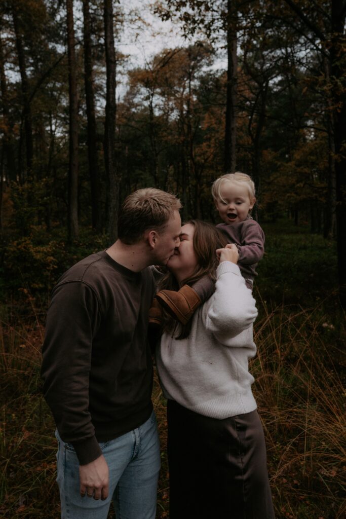 gezin in bos in Ede, vader geeft moeder een kus en meisje op schouders moeder