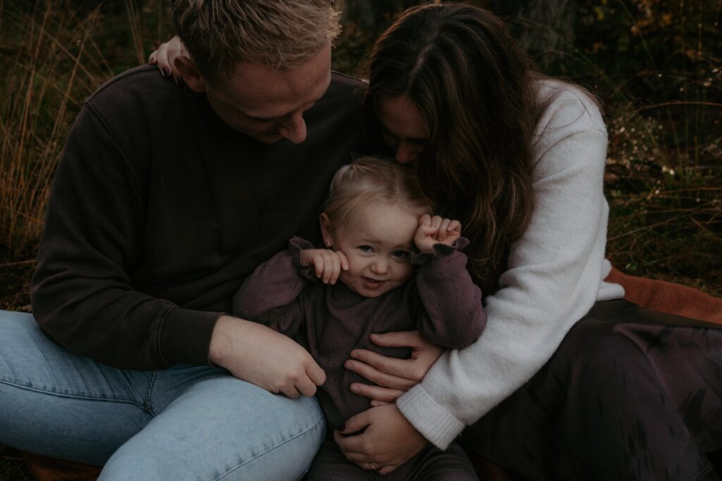 gezin in bos in Ede, meisje met ouders zitten bij elkaar en knuffelen