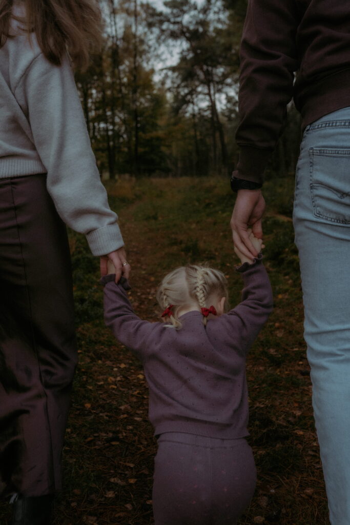 meisje houdt handen van papa en mama vast in bos in Ede