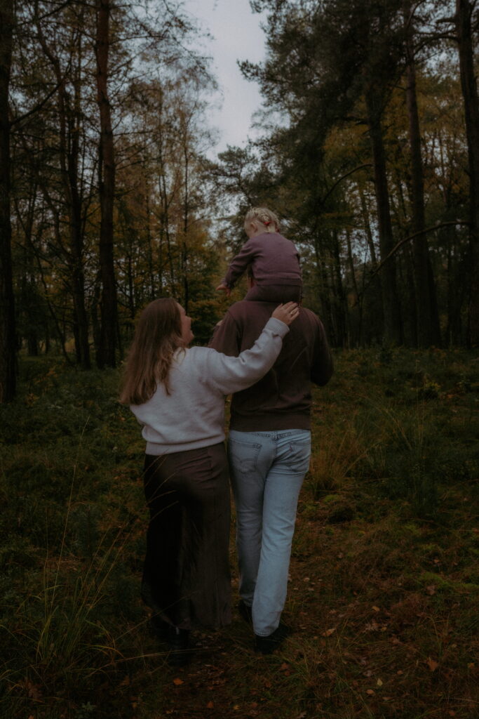 Vader en moeder lopen door bos in Ede met dochter op de schouders van papa