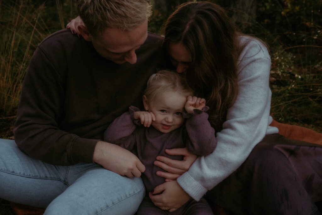 gezin in bos in Ede, meisje met ouders zitten bij elkaar en knuffelen