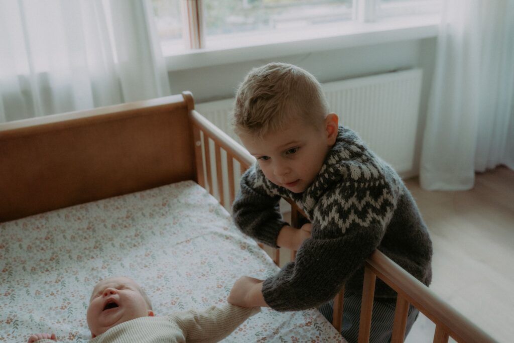 jongetje houdt handje van newborn zusje vast