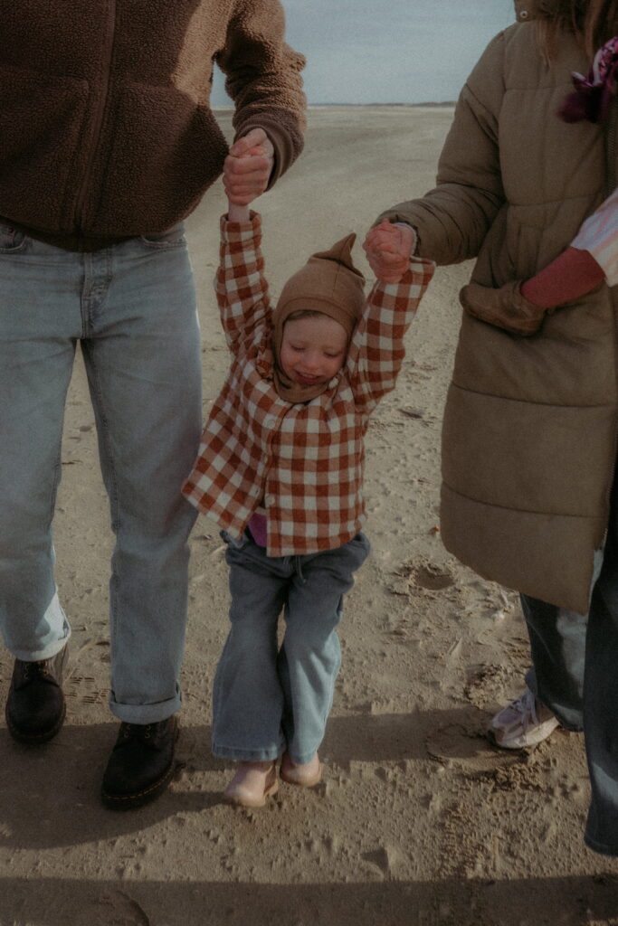 vader en moeder houden dochter vast en jonassen haar in het midden op het strand