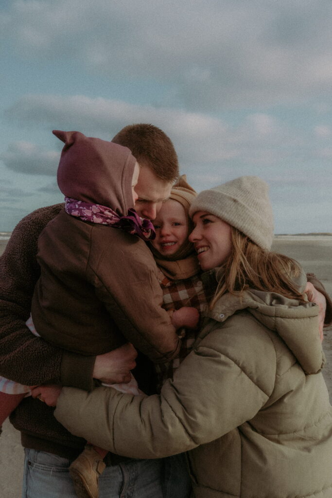 gezin met vader en moeder en twee dochters, knuffelen elkaar op het strand